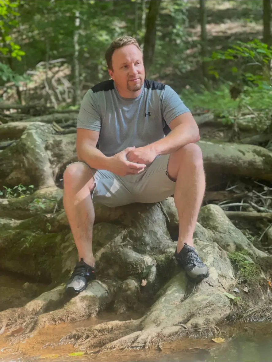 Travis Boles enjoying the outdoors, sitting by a creek in the woods