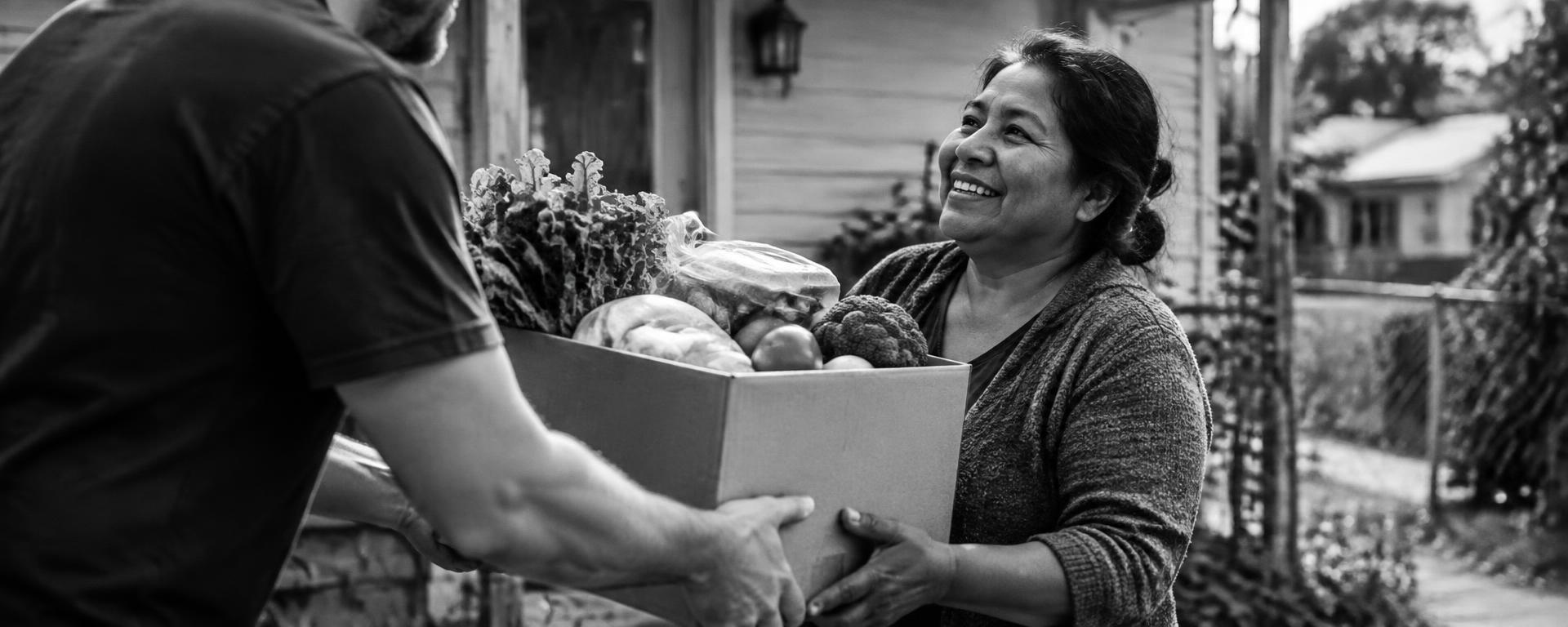 A volunteer handing a box of fresh groceries to a smiling neighbor